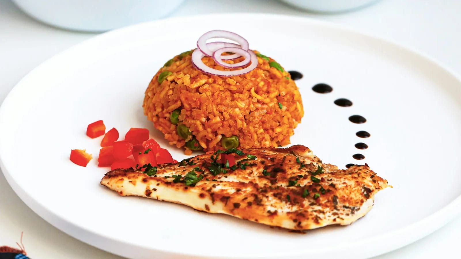 Riz djollof orangé dressé en assiette avec un filet de poisson grillé